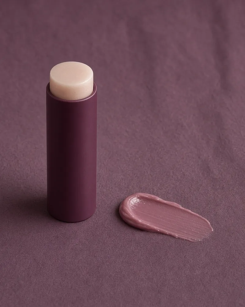 A plain balm and a cream smear on plum paper, no face in the frame.